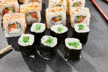 Maki sushi set on dark background. Maki set with variety rolls. Composition from popular sushi rolls and hosomaki. Style concept sushi menu with black background, leaves and hard shadow.