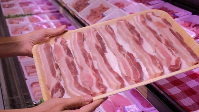 Close up of human hands holding package of delicious row bacon in butcher's supermarket, meat products 