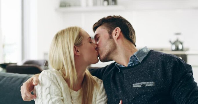 Young happy caucasian couple kissing on couch snuggling. Romantic young couple snuggling on couch kissing. Happy young couple hugging and kissing while relaxing on the couch