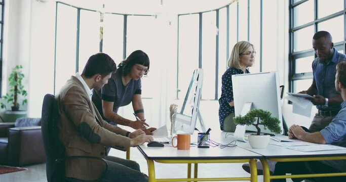 Getting everyone in on the project. Group of businesspeople at work in a modern office. Group of five diverse businesspeople working and talking around a desk in a modern office at work.