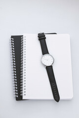 black leather watch on white work desk with black and white notebooks