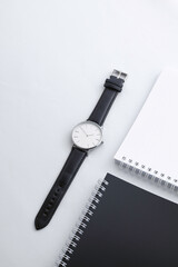 black leather watch on white work desk with black and white notebooks
