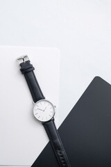black leather watch on white work desk with black and white notebooks