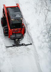 small tractor  with chains on wheels pushing snow with blade snow ploughing to clear walkway clearing snow from path in winter after heavy snowfall viewed from above vertical format room for type 