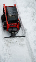 small tractor  with chains on wheels pushing snow with blade snow ploughing to clear walkway clearing snow from path in winter after heavy snowfall viewed from above vertical format room for type 