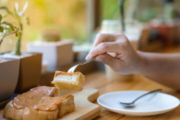 Close up to slices of toast bread and butter with steamed Thai tea custard topping in hand of woman using a fork to eat for breakfast. A hand eating delicious home made Thai tea Custard Toast dessert.