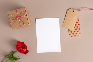 Valentine day,Mother day composition made of gift, red flower, label paper with hearts, white blank card on beige background. Flat lay, top view, copy space.