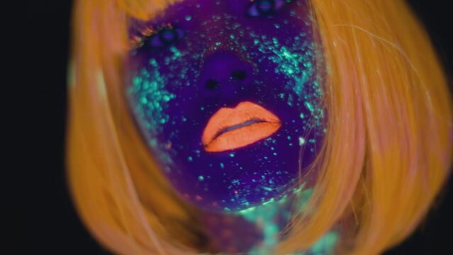 Close up portrait of young stylish asian woman pj with glowing make up and body art wearing orange wig dancing to camera