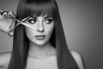 Beautiful young woman with a bright makeup and a smooth long hair holds metal scissors. Hair salon,...