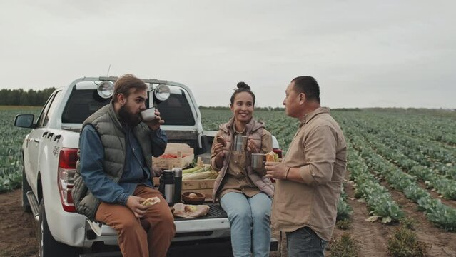 Group of three farm workers having lunch and chatting during break time after doing some work on field