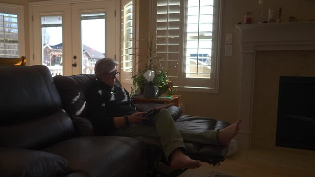 Senior retired woman reading on a tablet in her home at daytime - static wide angle view