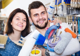 positive loving couple demonstrating tools for house renovating in paint supplies store