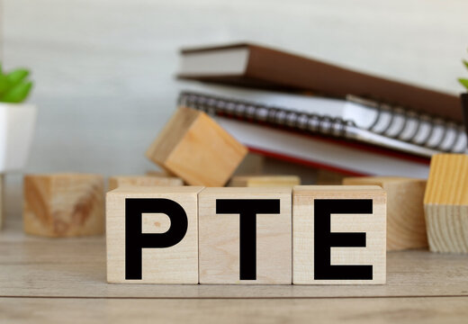 Pearson Tests of English PTE concept Foreign Language exams, text on wooden blocks on a working wooden table against the background of books and notepads. light background