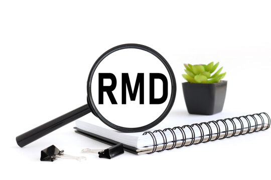 RMD Required Minimum Distributions white background black magnifying glass on a notebook near the plant and text on the glass
