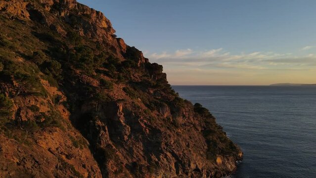 Drone footage of a sunset-lit, jagged-looking, seaside cliff along the coast of the Mediterranean Sea.