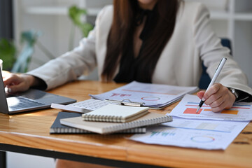 Businesswoman using laptop computer and checking financial reports at office desk.