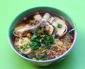 chicken noodles in a bowl placed on green background