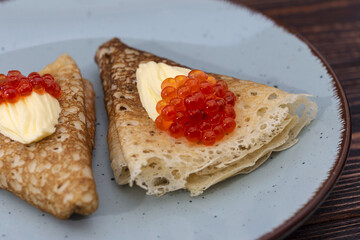 Pancakes with a piece of butter and  red caviar on a blue plate. Russian traditions, carnival. Top view, place for text.