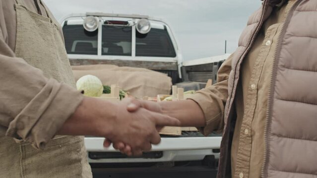 Unrecognizable woman buying vegetables at farmers standing in front of farm owner discussing something and doing handshake