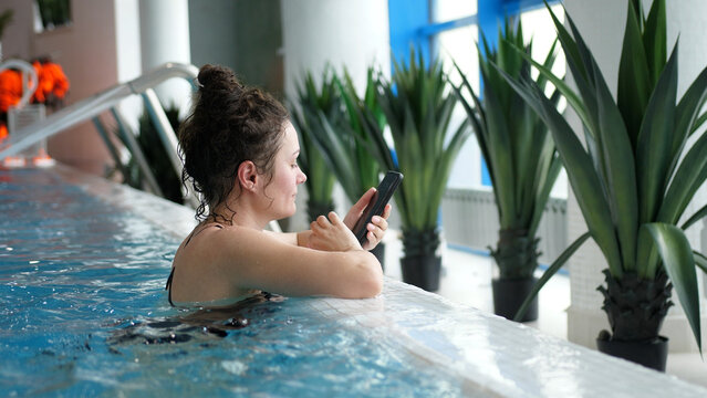 Young woman in a swimming pool uses cellphone.