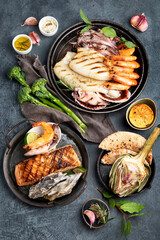 Grilled fish and seafood assortment on dark background.