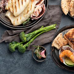 Grilled fish and seafood assortment on dark background.