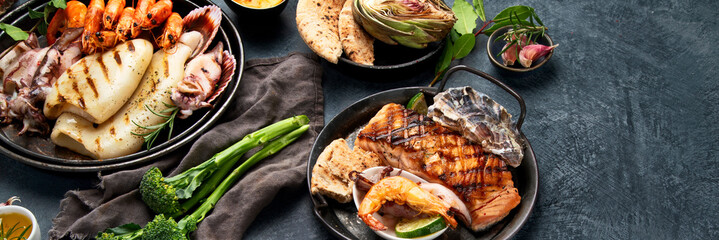 Grilled fish and seafood assortment on dark background.