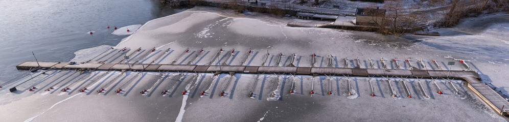 Top view over the icy lake Mälaren with jetty floating arms with buoys at an icy bay of the lake...