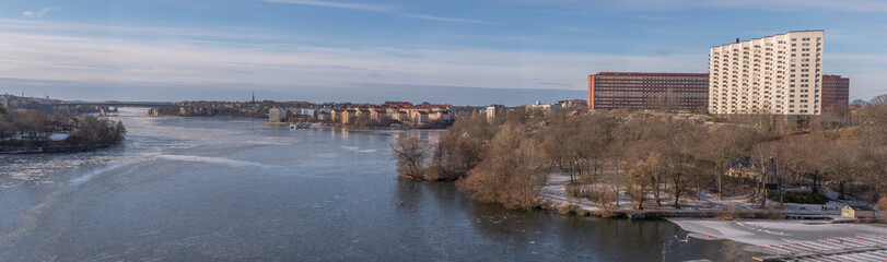 Panorama view over the islands Kungsholmen and Lilla Essingen, and a icy bay of the lake Mälaren with apartment houses, jetties and bridges a cold sunny winter day in Stockholm