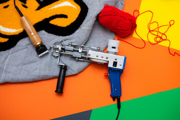 A tufting gun with multicolored yarns against a bright colored background. - 484570600