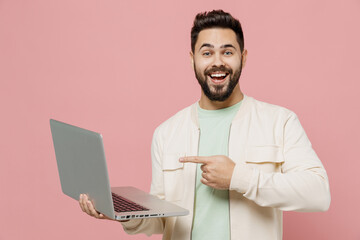 Young smiling happy cheerful man 20s wear trendy jacket shirt hold use work point finger on laptop...