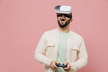 Young happy man 20s wear trendy jacket shirt hold in hand play pc game with joystick console watching in vr headset pc gadget isolated on plain pastel light pink background. People lifestyle concept.