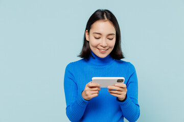 Fototapeta premium Young woman of Asian ethnicity 20s wears blue shirt using play racing app on mobile cell phone hold gadget smartphone for pc video games isolated on plain pastel light blue background studio portrait.