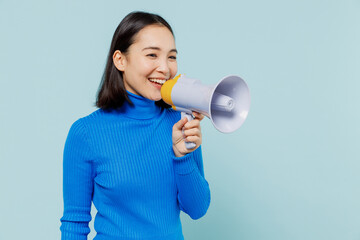 Promoter vivid young woman of Asian ethnicity 20s years old wears blue shirt hold scream in megaphone announces discounts sale Hurry up isolated on plain pastel light blue background studio portrait.