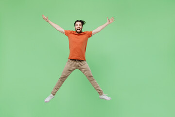 Full body young excited fun man 20s wear casual orange t-shirt jump high with outsretched hands legs isolated on plain pastel light green color background studio portrait. People lifestyle concept