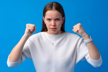 Young annoyed angry woman holding hands in furious gesture on blue background