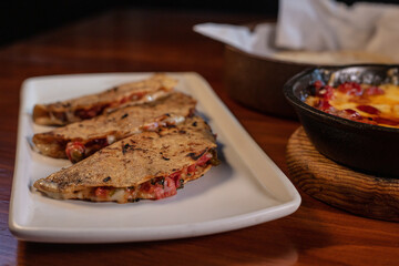 Three quesadillas on a white plate next to mexican food