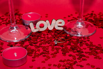 Wedding ring, wooden word love, small red candles and red confetti on a red background