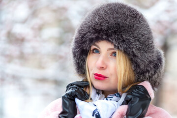 happy woman in a pink faux fur coat in winter on a background of snowy trees
