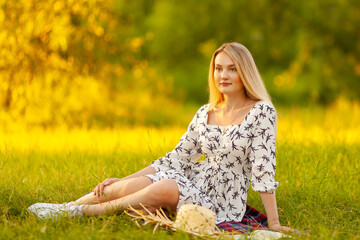 blonde woman in a light dress resting on the grass in summer