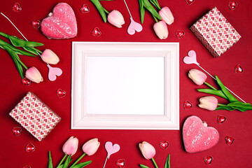 Empty white photo frame with tulips flowers, gifts and hearts on red background.