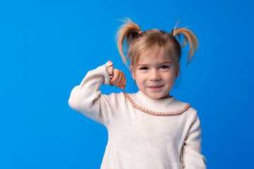 Little cute girl showing her strength against blue background