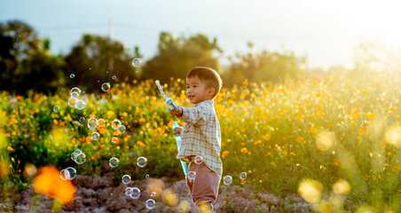 Little Asian boy playing soap bubbles enjoying in the flower garden at sunset.