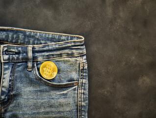 blue jeans with a pocket and a gold bitcoin coin on a gray background.  electronic virtual money.