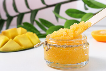 Homemade cosmetic product with mango and green leaves of the plant on the background. Scrub them with sugar for peeling and hygiene procedures.