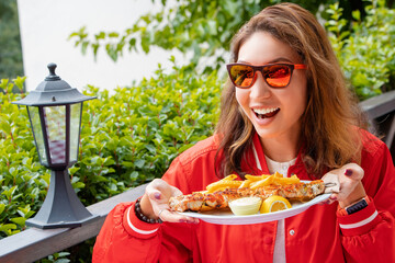 Smiling girl eating traditional Greek grilled meat - souvlaki with french fries. Fastfood and...