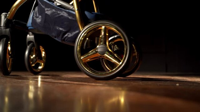 Lower part of dark blue baby stroller with golden elements. Modern perambulator on the smooth floor in the dark room.