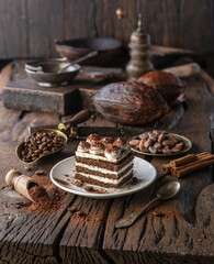 Slice of chocolate cake with tiramisu cream and cocoa powder on wooden table.