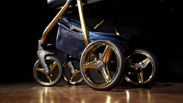 Nice modern baby stroller with shining golden elements in wheels. Baby pram being shaken in the dark room.