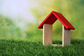 Miniature house on green grass with sunlight background. Copy space for text. Eco house concept